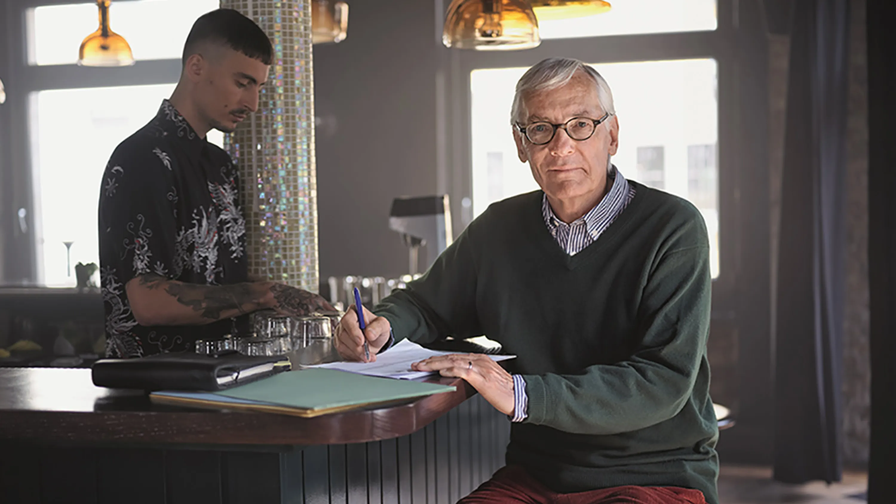Un uomo anziano siede al bar di un caffè e controlla i documenti.